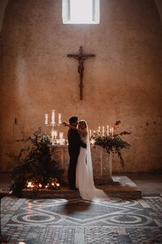 a man and woman standing in front of a cross with candles on the altar behind them