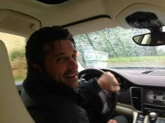 a man sitting in the driver's seat of a car with his hand on the steering wheel