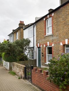 a brick house with white windows and green door, next to a sidewalk in front of it