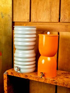 an orange and white vase sitting on top of a wooden shelf next to a stack of stacked plates