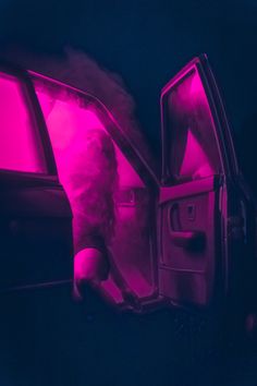 a person is opening the door of a car with pink light coming from behind it