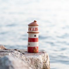 a red and white lighthouse sitting on top of a rock next to the ocean with water in the background