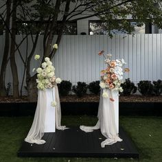 two tall white vases filled with flowers sitting on top of a black platform in the grass