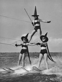 three women in bikinis on water skis wearing witch hats and holding hands with each other