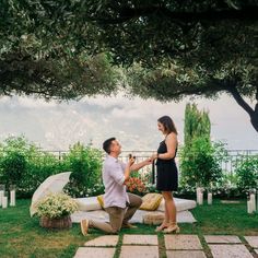 a man kneeling down next to a woman on top of a lush green field with trees