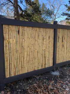 a fence made out of bamboo sticks in front of some trees and bushes with no leaves on the ground