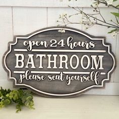 a bathroom sign sitting on top of a white shelf next to a potted plant