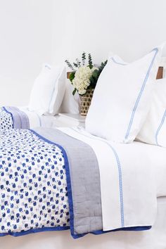 a bed with white and blue sheets, pillows and a basket full of flowers on it