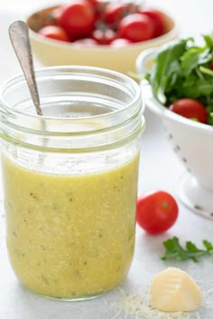 a glass jar filled with dressing next to a bowl of tomatoes and lettuce