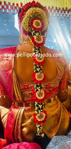 a woman wearing a red and gold sari with flowers in her hair is sitting down