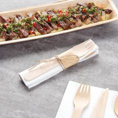 a wooden plate with meat and vegetables on it next to utensils, napkins and forks