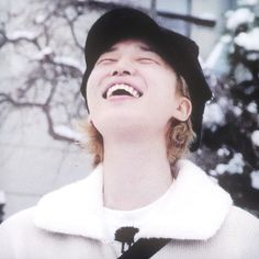 a woman laughing while wearing a hat and coat in front of snow covered tree branches