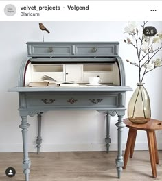 an old desk has been painted blue with white flowers in vase and bird on top