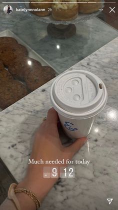 a person is holding a coffee cup in front of doughnuts on the counter