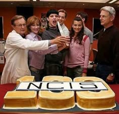 a group of people standing in front of a cake with the word ncis on it