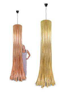 a woman is standing next to two tall wooden lamps that are shaped like long strips of wood