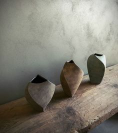 three ceramic vases sitting on top of a wooden table next to each other in front of a gray wall