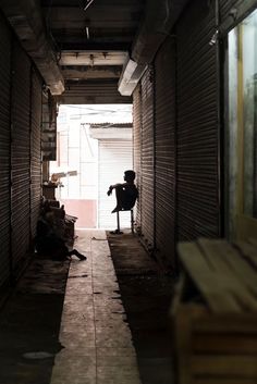 a person sitting on a chair in the middle of a long hallway with brick walls