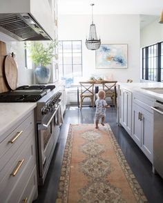 a toddler standing in the middle of a kitchen with an area rug on the floor