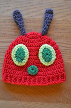 a crocheted red hat with two green eyes on top of a wooden table