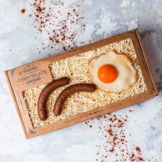 an egg and sausage in a cardboard box on a white surface with brown sprinkles