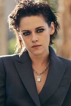 a woman wearing a suit and necklace with a padlock on her chest looking at the camera