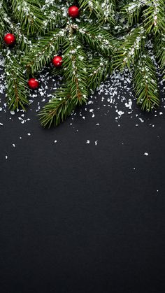 christmas tree branches covered in snow and red ornaments