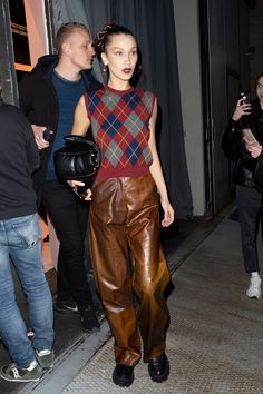 a woman in brown leather pants is walking down the street with her hand on her hip