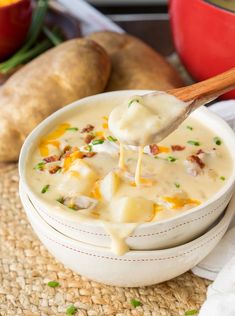 a spoon full of potato soup with cheese and bacon on top, in a white bowl