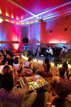 a group of people sitting on the floor in a room with candles and lights around them