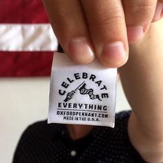 a person holding up a tag that says celebrate everything except the american flag in the background