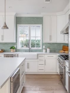 a kitchen with white cabinets and green tile backsplash, stainless steel appliances and wood flooring