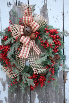 a christmas wreath hanging on the side of a wooden door with red berries and pine cones