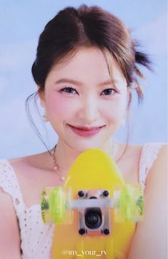 a girl holding a yellow skateboard in front of her face and smiling at the camera