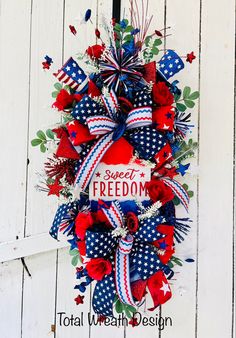 a patriotic wreath hanging on the side of a white wooden door with red, white and blue decorations