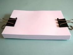 a binder with two clips attached to it sitting on a blue table top next to a pair of scissors