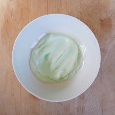 a white bowl filled with green cream on top of a wooden table