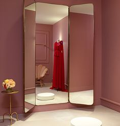 a room with a mirror, table and chair in it that has a red dress on the mannequin