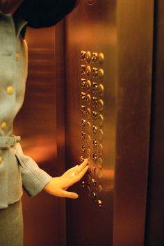 there is a doll that is standing in front of the elevator door and holding her hand out