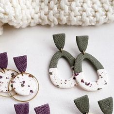 several different types of earrings are laying on a white surface next to a knitted blanket