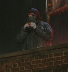 a person wearing a face mask while standing on a brick wall looking at something in the distance