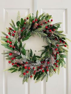 a christmas wreath hanging on the front door with pine cones and red berries, greenery and holly