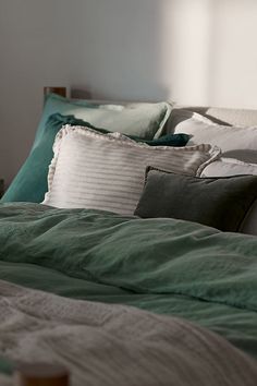 an unmade bed with green and white pillows