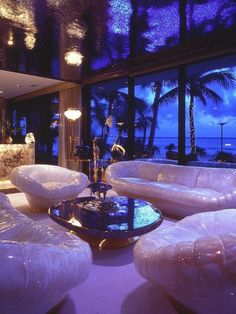 a living room filled with white furniture and large windows overlooking the ocean at night time