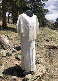 a white dress with fringes on it sitting in the grass next to some trees