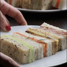 a person is holding a plate with sandwiches on it and another one has a red manicure