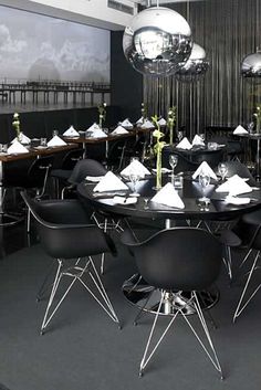 a dining room with black tables and chairs, silver chandeliers hanging from the ceiling