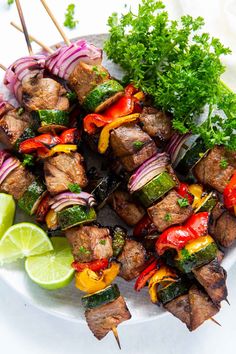 skewered meat and vegetables on a plate with lime wedges