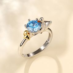 a ring with a blue topazte surrounded by gold and silver accents on a white background