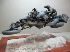 a model of a motorcycle is displayed on a wooden stand with white sand and rocks